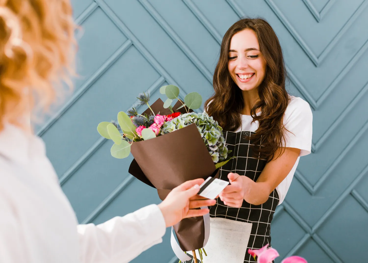 Un artisan fleuriste prépare un bouquet de saison sur son établi avant une livraison, avec des tiges encore en boutons et un emballage protecteur.