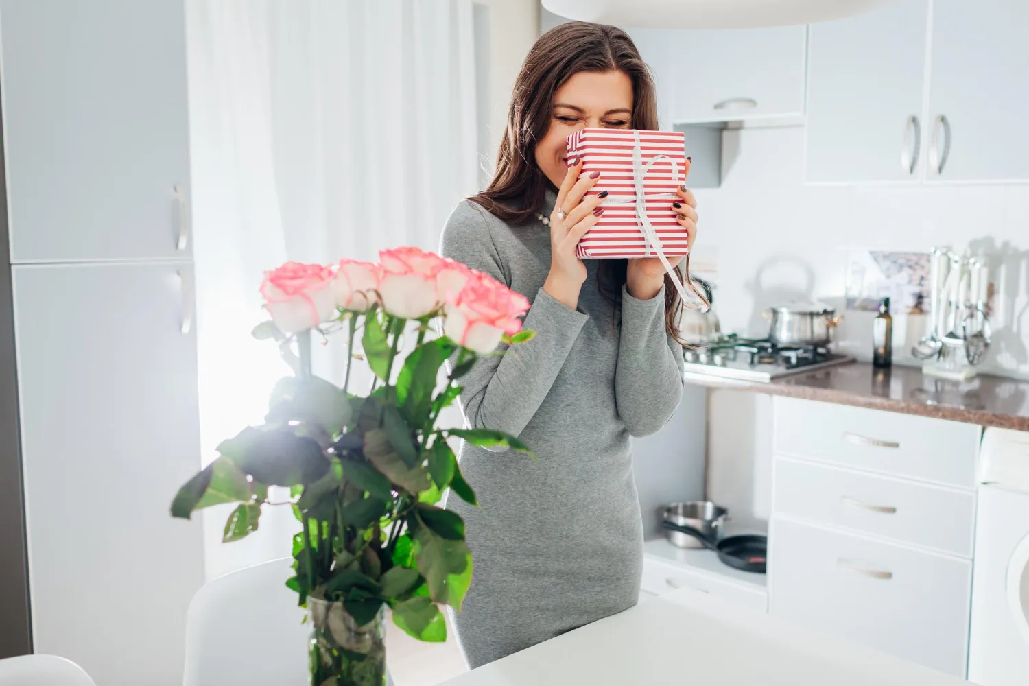 Un bouquet de Saint-Valentin composé de roses, tulipes et renoncules fraîches dans un vase, posé sur une table lumineuse près d’un mot manuscrit.